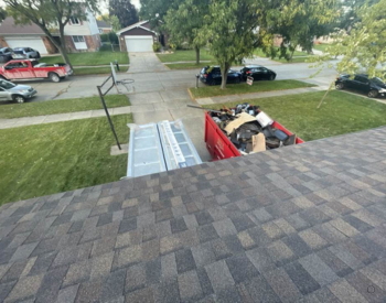Shelby Township, MI, suburban neighborhood with a red dumpster full of waste gets new asphalt roofing shingles.